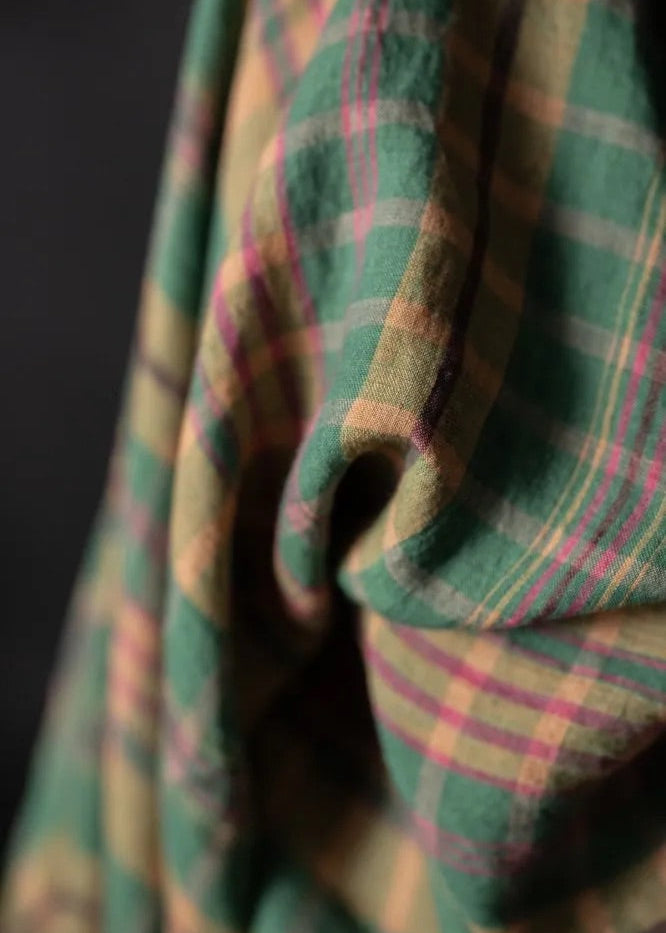 Close-up of a plaid fabric with green, pink, and brown colors on a dark background.