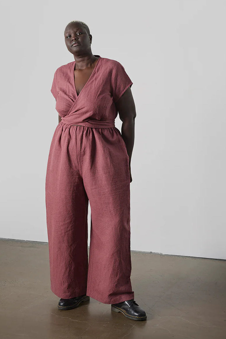 Person wearing a pink jumpsuit standing against a plain white wall.
