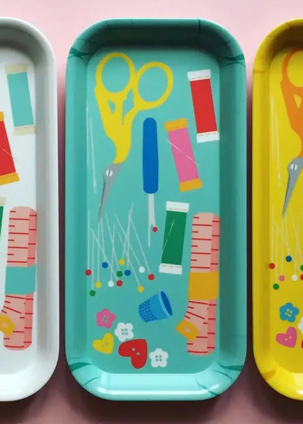 Four colorful trays with scissors and thread illustrations on a pink background