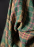 Close-up of a plaid fabric with green, pink, and brown colors on a dark background.