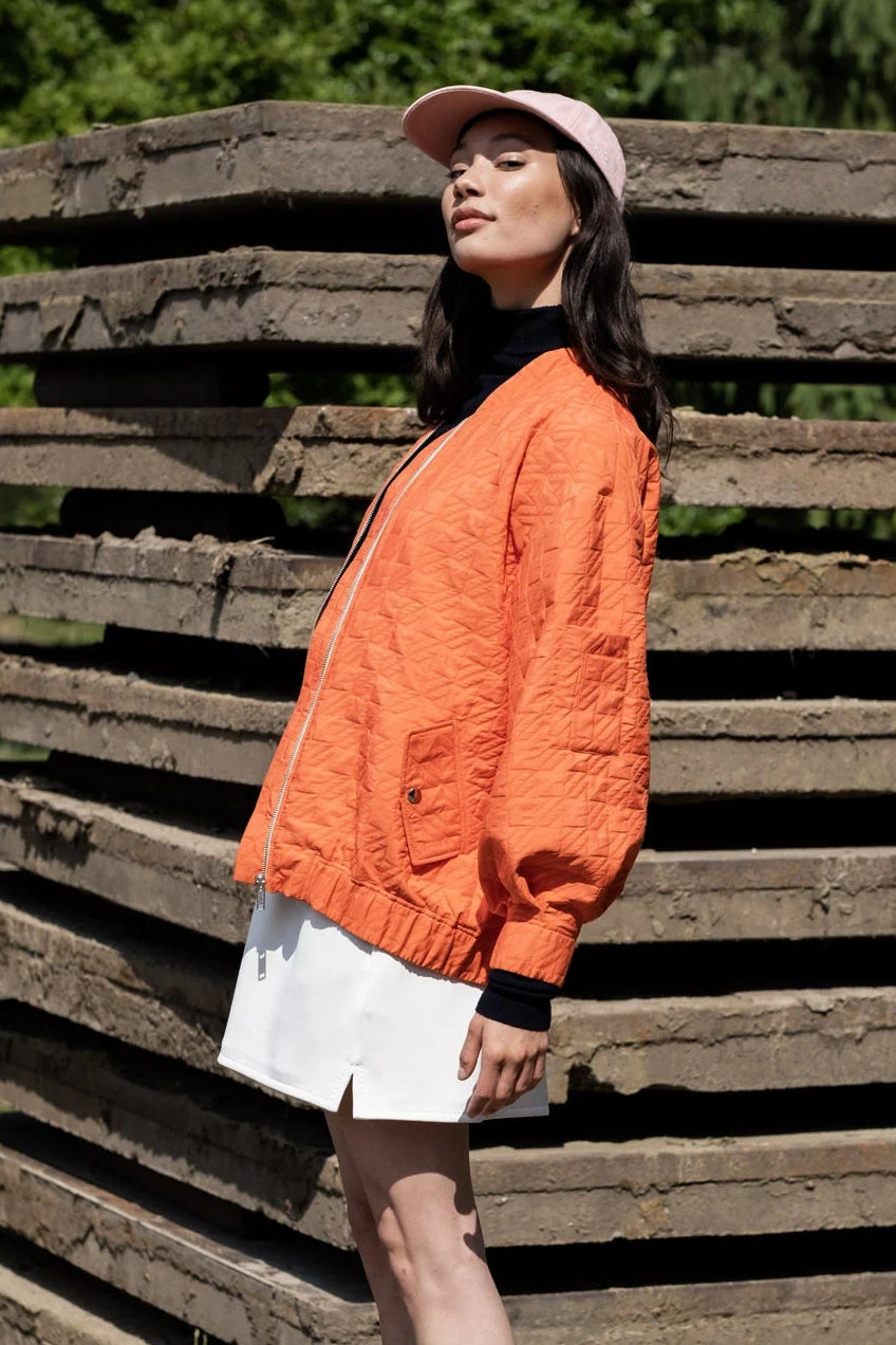 Person wearing an orange sweater and white shorts standing in front of wooden pallets.
