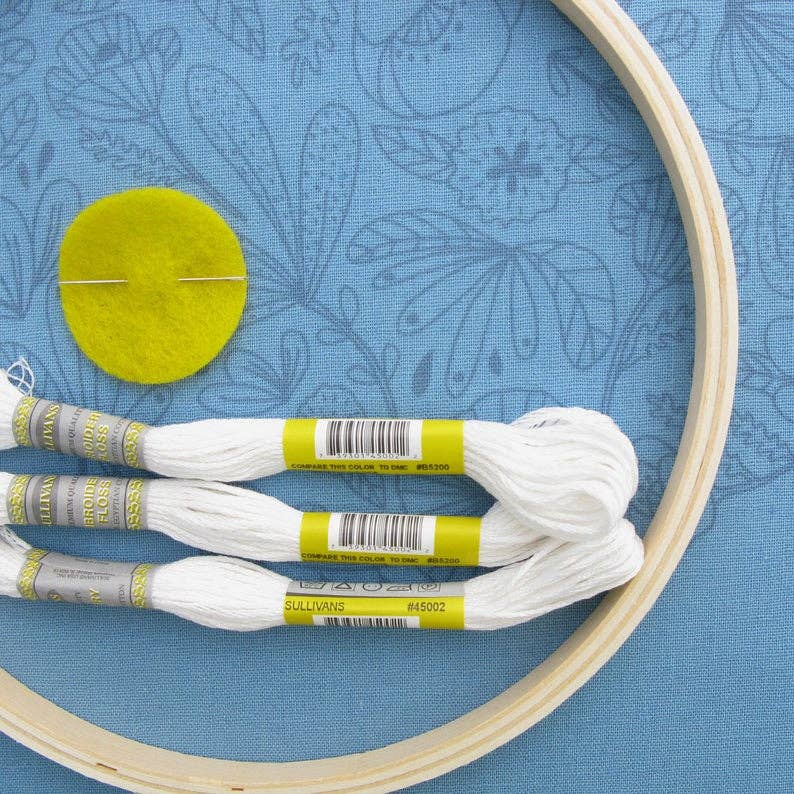 Embroidery hoop with thread and a yellow felt circle on a blue floral fabric background