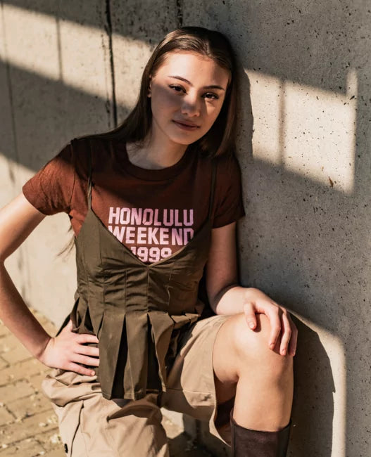 Person wearing a 'Honolulu Weekend 1999' t-shirt against a concrete wall.