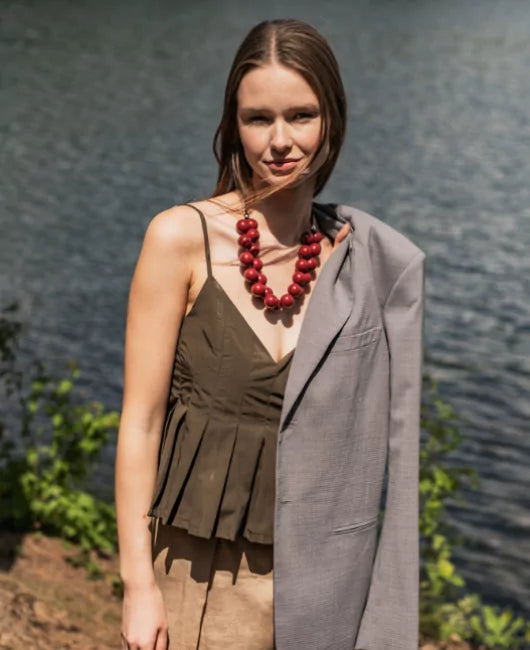Woman wearing a green dress and red necklace with a gray coat over her shoulder, standing outdoors.