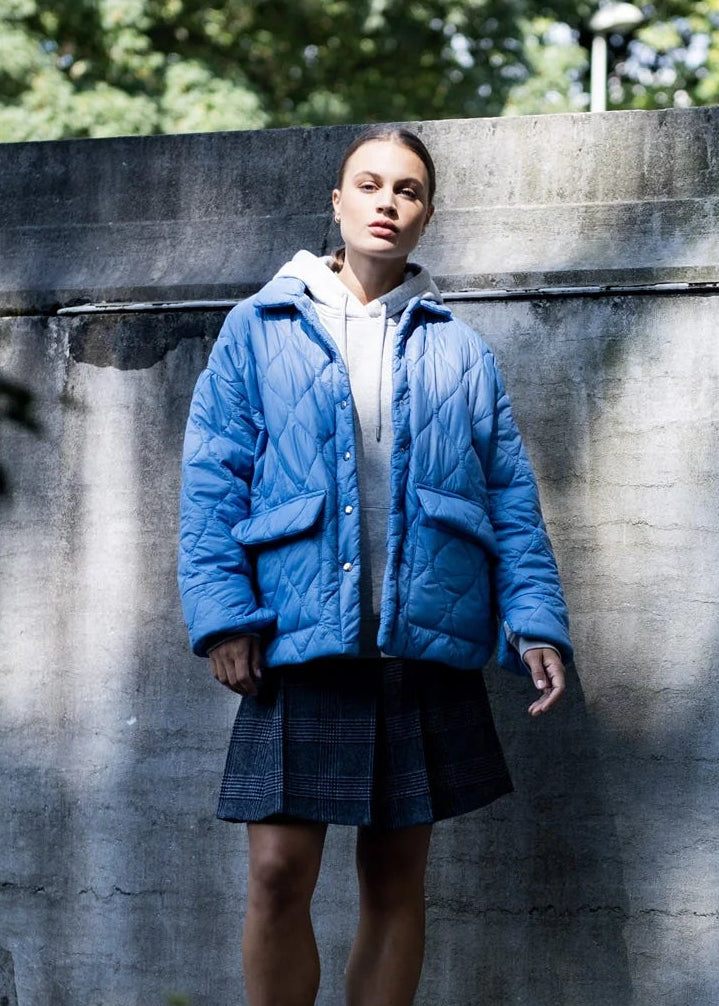 Person wearing a blue jacket standing against a stone wall with trees in the background