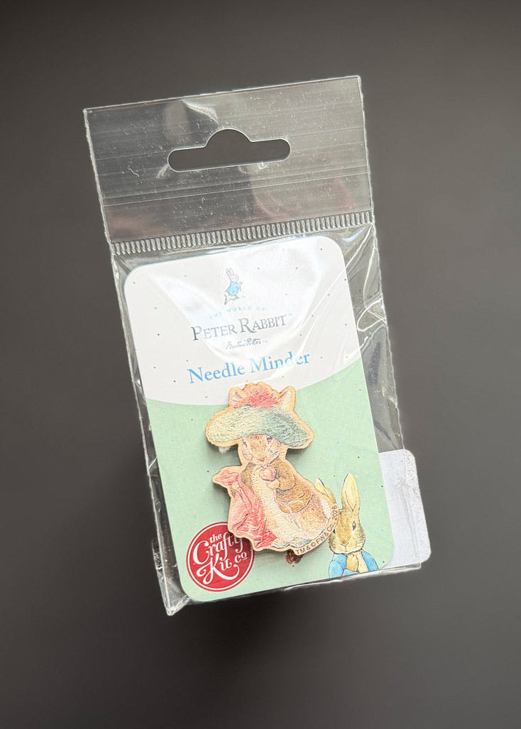 A Peter Rabbit Needle Pin set in its original clear plastic blister packaging, displayed against a dark gray background.