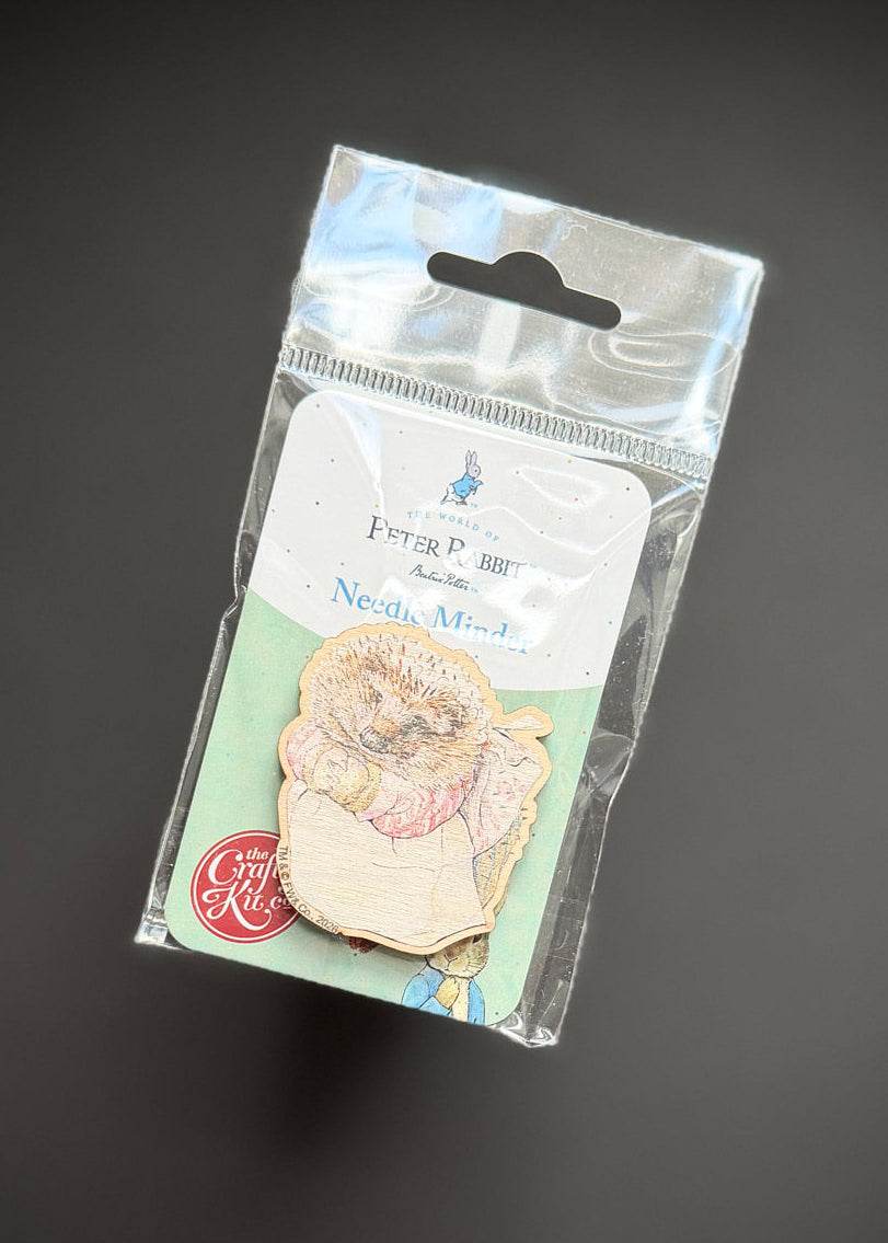 A packaged enamel pin featuring a teddy bear holding a pink flower, attached to a white and mint backing card inside a clear plastic hanging bag, photographed on a dark gray background.