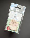 A packaged enamel pin featuring a teddy bear holding a pink flower, attached to a white and mint backing card inside a clear plastic hanging bag, photographed on a dark gray background.