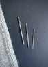 Three metal knitting needles on a dark surface with a knitted fabric corner.